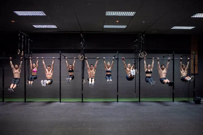 Male and female athletes hanging on rod at gym