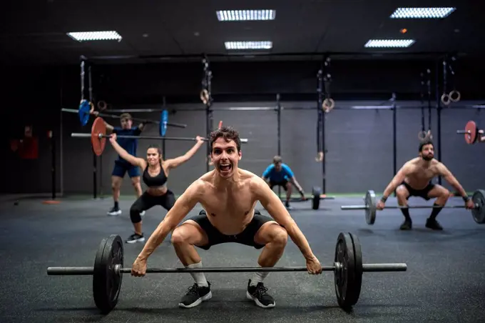 Athletes picking barbell while exercising at gym