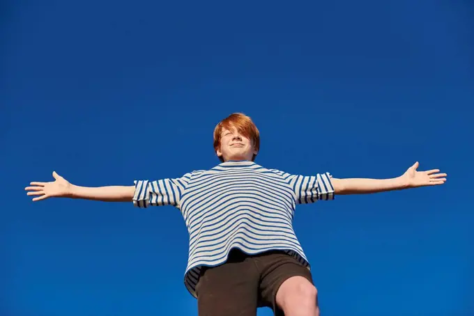 Boy standing with arms outstretched against clear sky