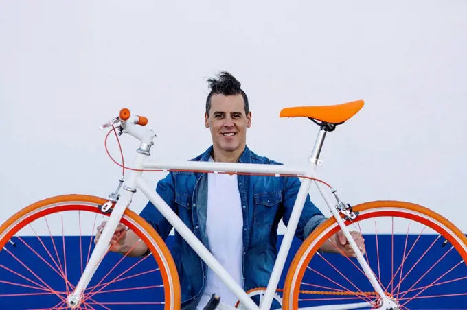 Smiling handsome man carrying orange bicycle against white wall