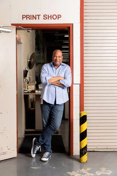 Smiling supervisor with arms crossed leaning on doorway at print shop