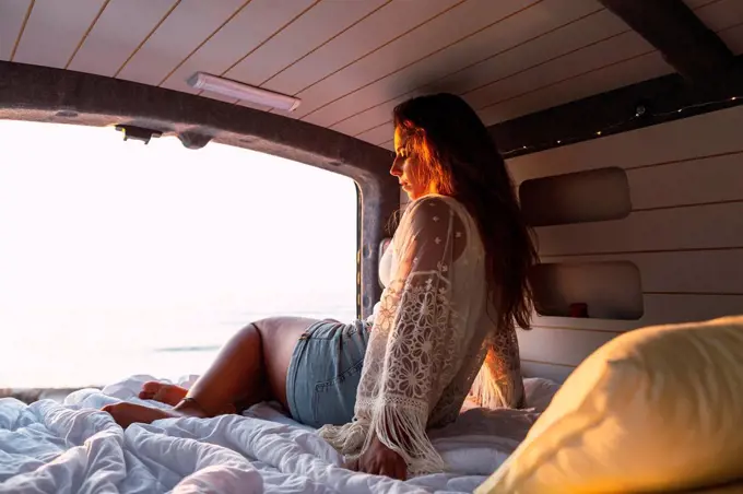 Woman sitting in camper van during sunset at beach