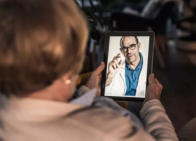 Mature male doctor showing medicine to senior patient on video call at home