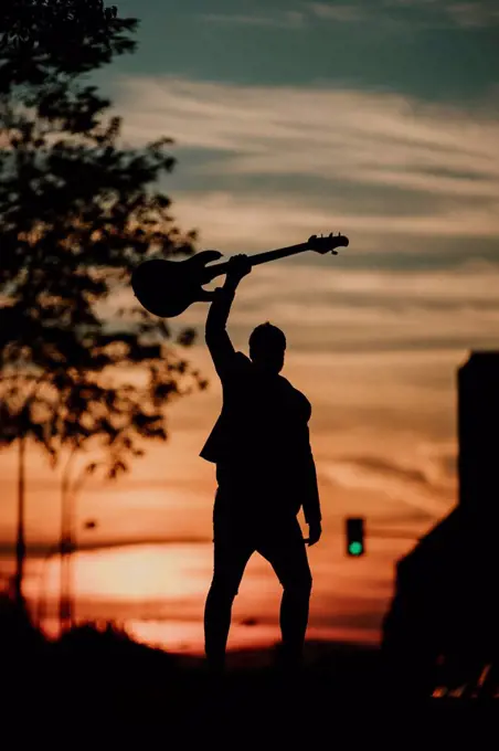 Musician holding bass guitar while standing on road during sunset