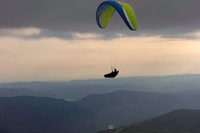 Aerial view of male paraglider soaring above mountains at dusk