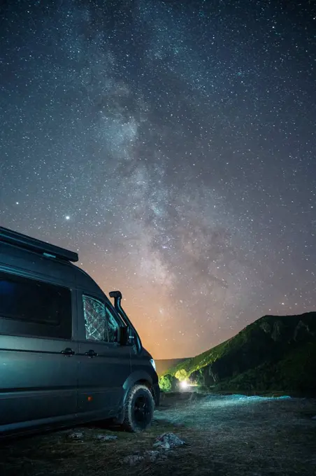 Camper van parked near mountain against star sky