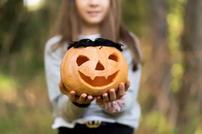 Girl holding Halloween pumpkin while standing at park