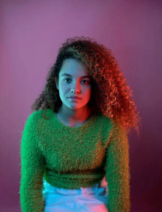 Red light on fashionable woman with curly hair sitting against pink background