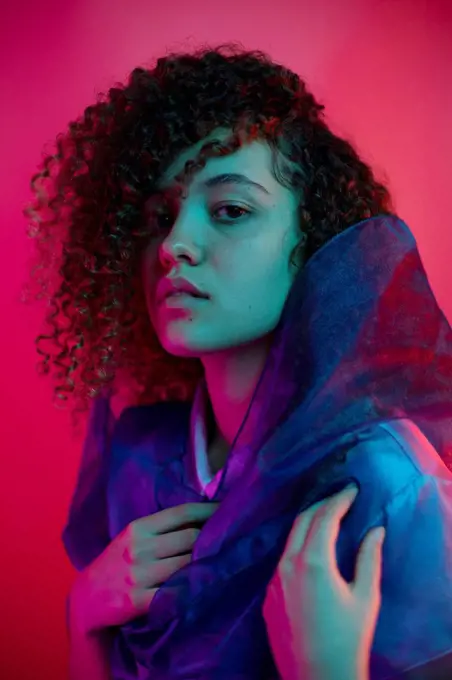 Beautiful woman with curly hair wearing scarf against pink background