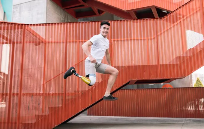 Young disabled man jumping against orange staircase