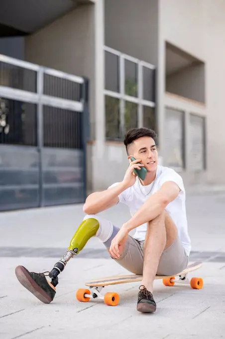 Young disabled man talking through mobile phone while sitting on skateboard