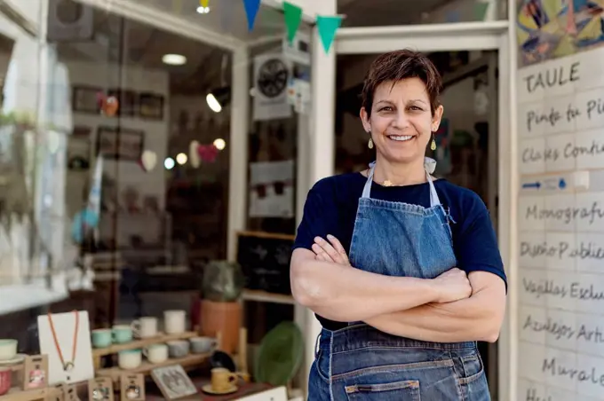 Happy small business owner standing with arms crossed outside her store