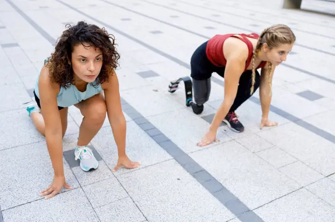 Sportswoman crouching by amputee for sports race on footpath