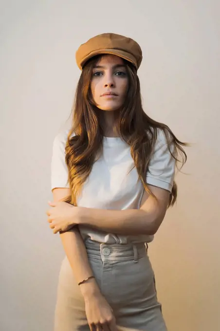 Woman wearing cap staring while standing against wall