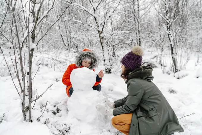 Girl with teenage sister making snowman in forest