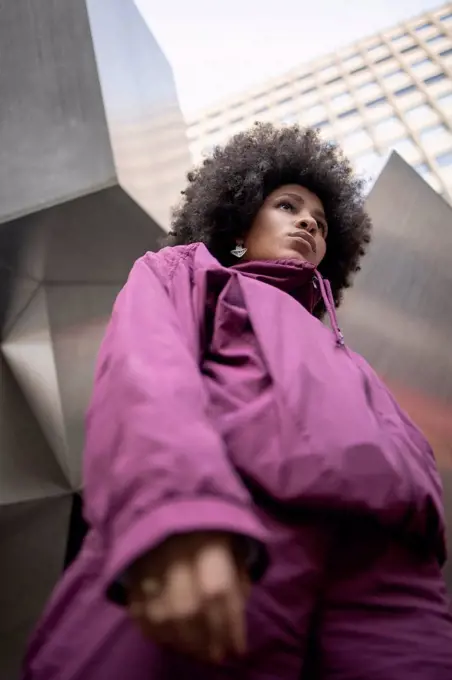 Afro young woman in warm clothing contemplating against built structure