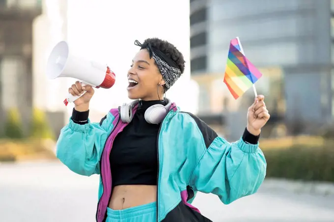 Female LGBTQIA protestor holding rainbow flag while announcing through megaphone