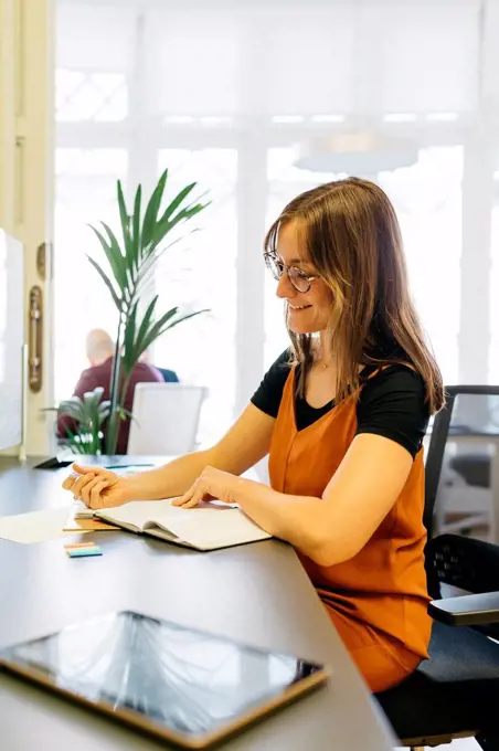 Smiling businesswoman reading diary at office desk