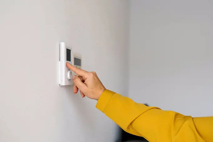 Mature woman adjusting thermostat at home