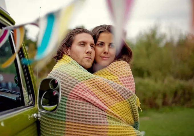 Young man and woman wrapped in blanket embracing each other
