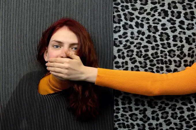 Studio shot of female hand covering mouth of young redhead woman
