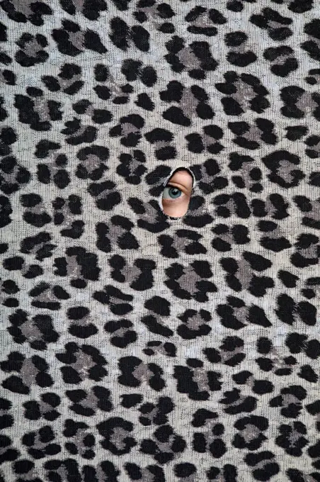 Eye of teenage girl peeking through hole in leopard print pattern