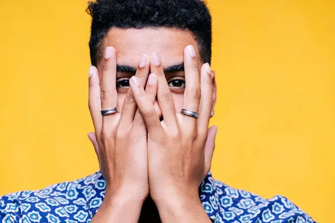 Man covering face with hands against yellow background
