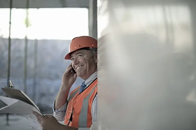 Smiling male architect talking on smart phone at construction site