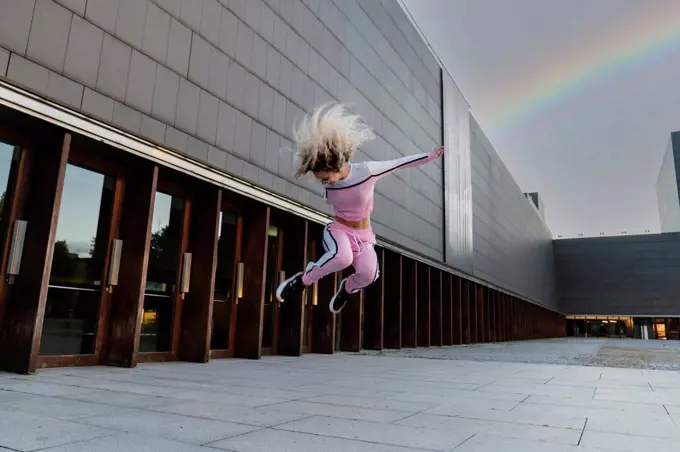 Cheerful woman jumping on footpath against building