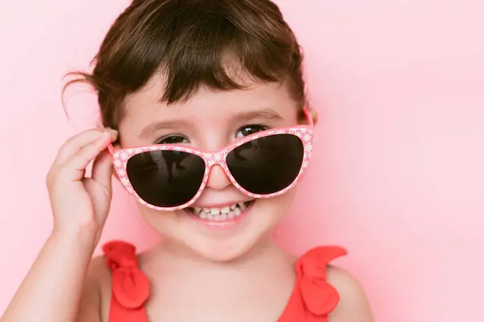 Portrait of happy little girl wearing sunglasses against pink background