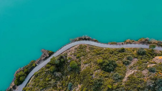 Aerial view of country road stretching along shore of turquoise lake