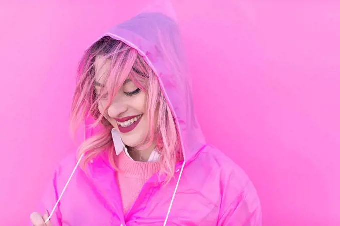 Happy woman with pink hair wearing raincoat in front of wall