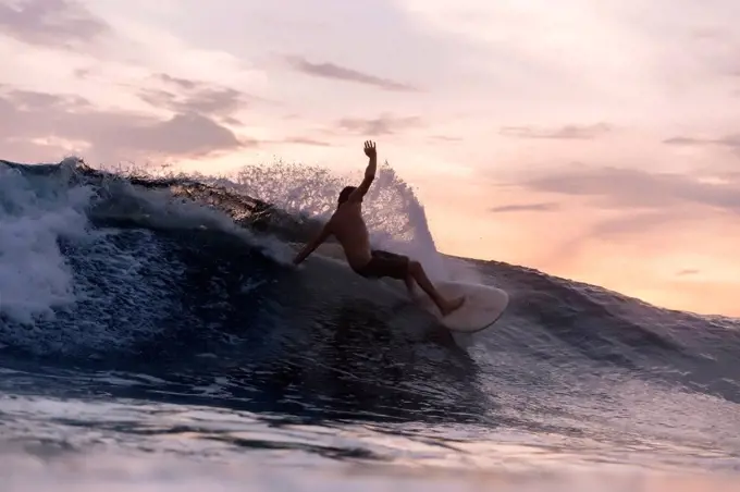 Tourist surfing over waves in sea during sunset