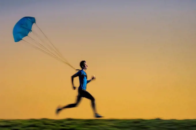 Male sportsperson jogging with parachute during sunset