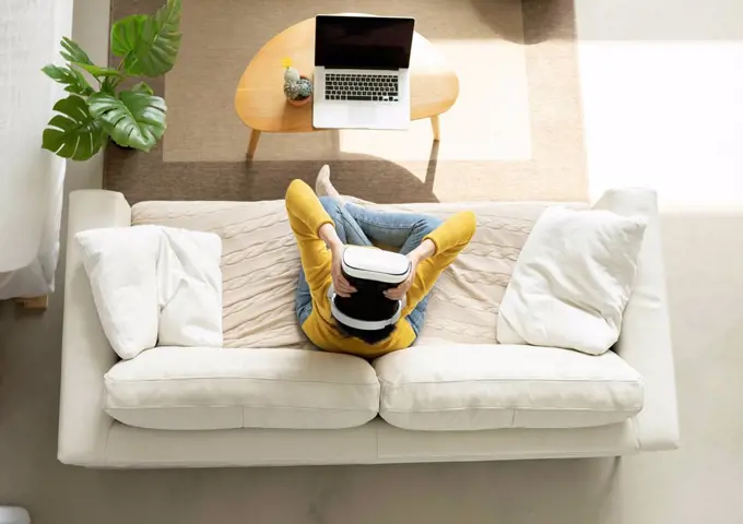 Woman holding Virtual reality headset while sitting on sofa at home