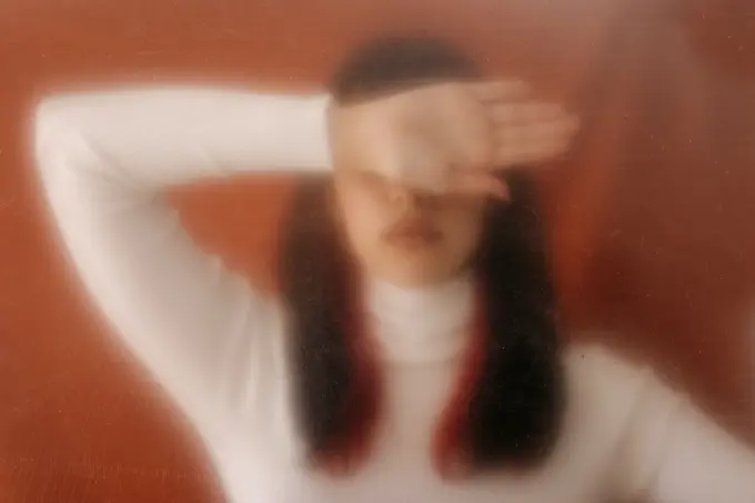 Young woman covering eyes with hand behind plastic sheet