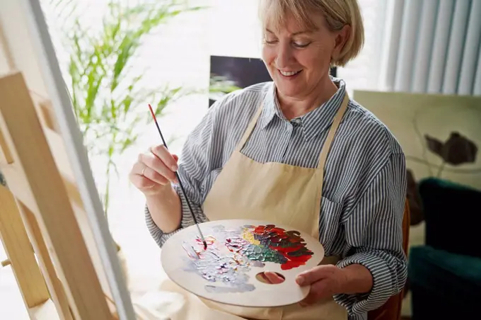 Smiling woman mixing colors while making painting at home