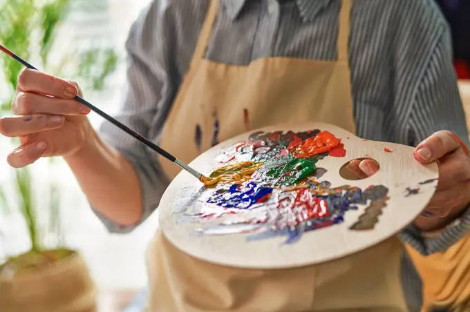 Woman holding palette while mixing colors through paintbrush at home