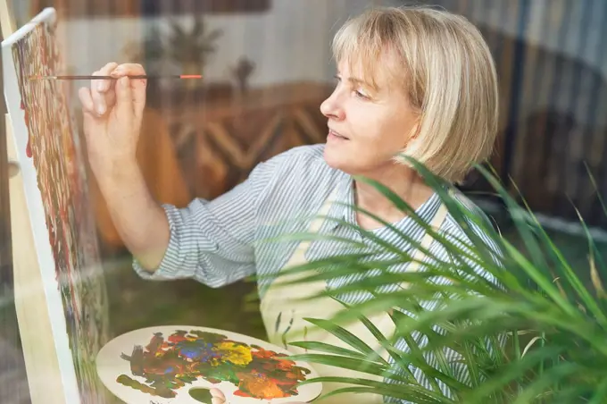 Mature woman with blond hair painting on easel at home