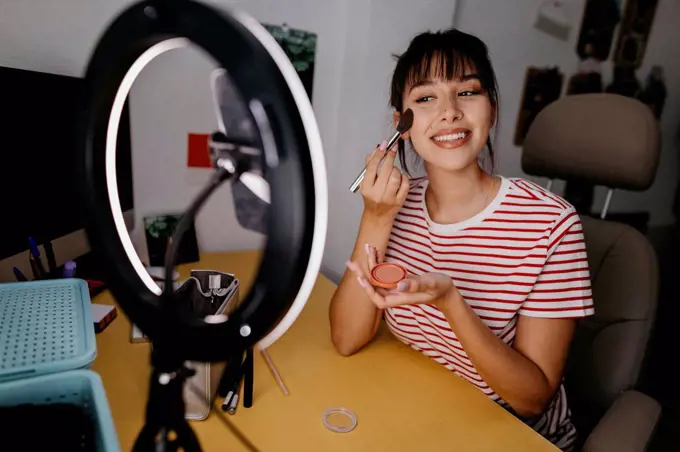 Female influencer vlogging while applying make-up at studio