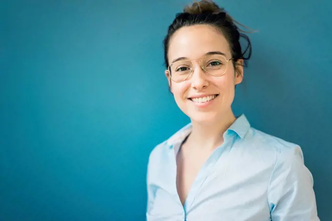 Portrait of smiling young woman wearing glasses in front of blue wall