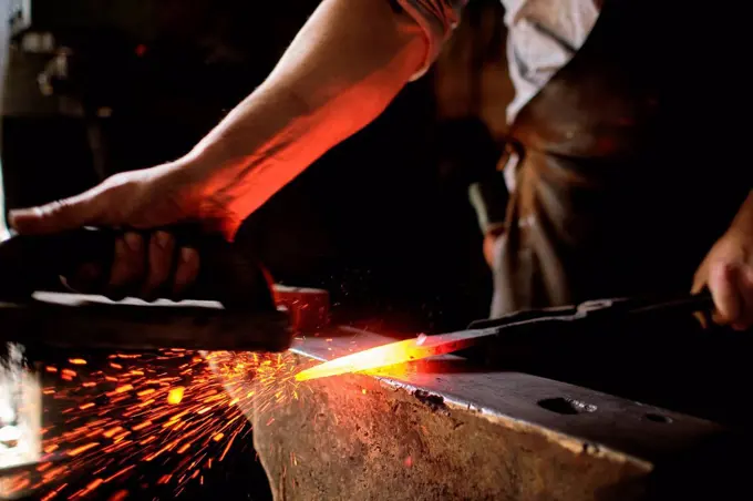 Male expert forging overheated metal on anvil at blacksmith shop