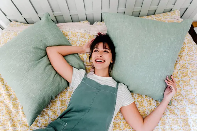 Thoughtful woman smiling while lying on bed