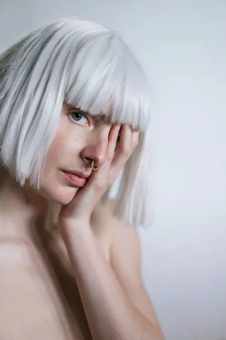 Woman with white hair covering eye with hand in front of white wall