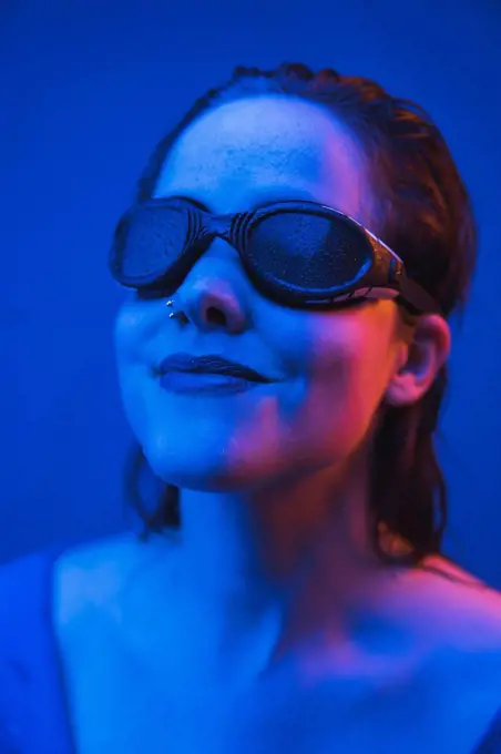 Beautiful woman wearing swimming goggles in front of blue background