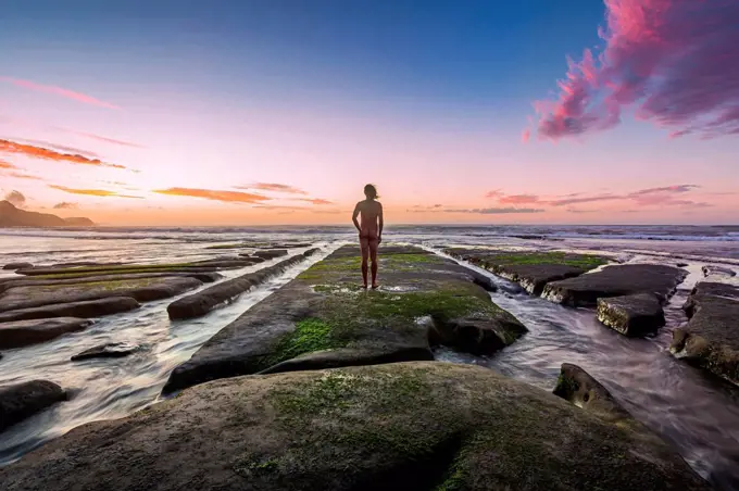 New Zealand, North Island, Rear view of naked man looking at ocean at sunset