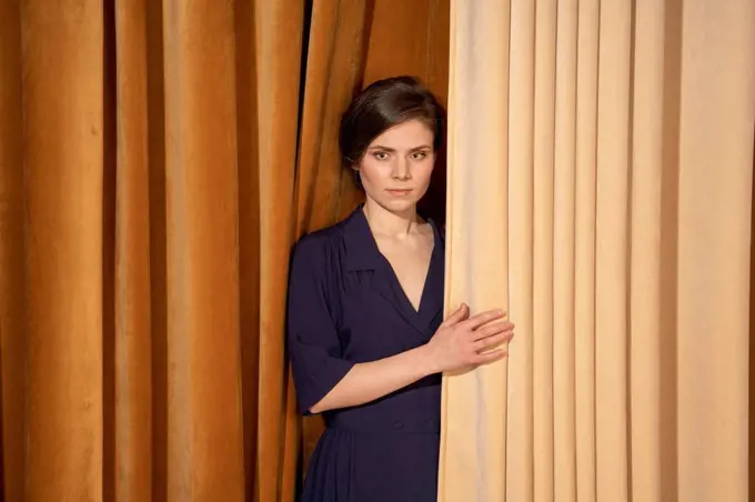 Confident young woman standing by curtain