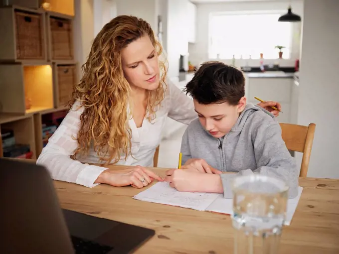 Mother teaching while son writing at home