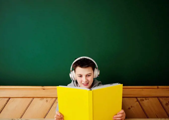 Boy wearing headphones while reading book at home