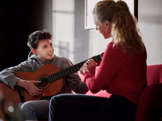 Mother assisting son plying guitar at home